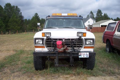 1973 Ford F-250 - Front view of a white Ford F-250 pickup truck equipped with a snow plow attachment and amber light bar. A red pickup truck is parked to the…