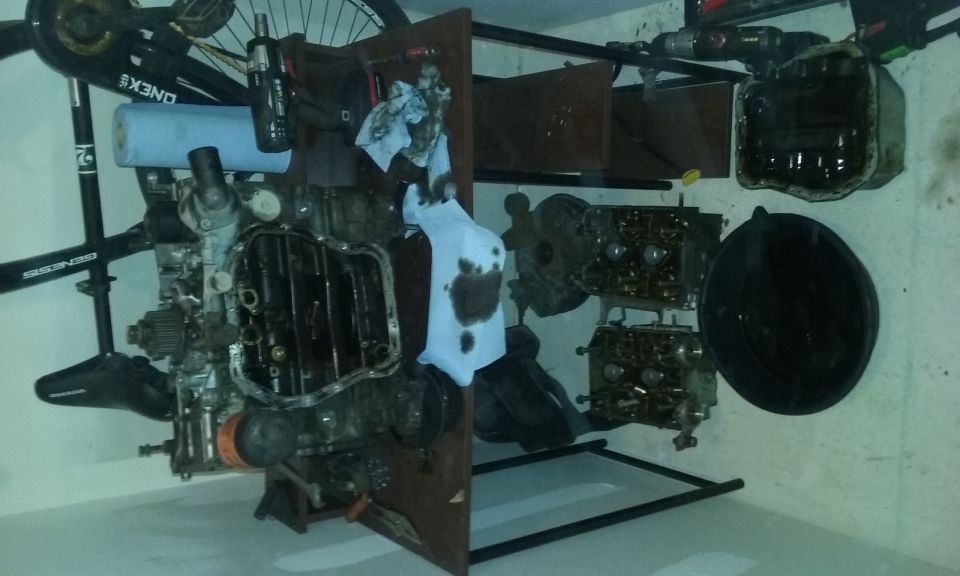 Disassembled engine and parts in a garage, with a bicycle in the background.