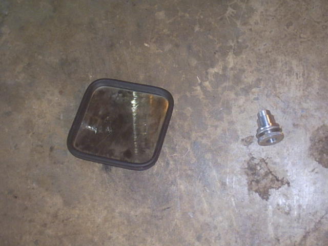 Side mirror glass with black trim and a small metal fitting on a concrete floor