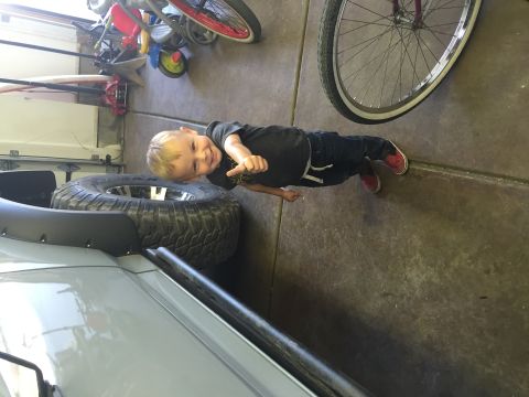 1988 Ford Bronco - A young boy in a dark t-shirt and jeans poses in front of a spare tire mounted on what appears to be a vehicle. The scene is indoors, likel…