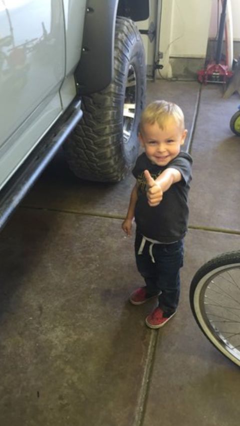 1988 Ford Bronco - A young boy gives a thumbs-up while standing next to the large tire and fender flare of a lifted vehicle. The scene appears to be a garage…