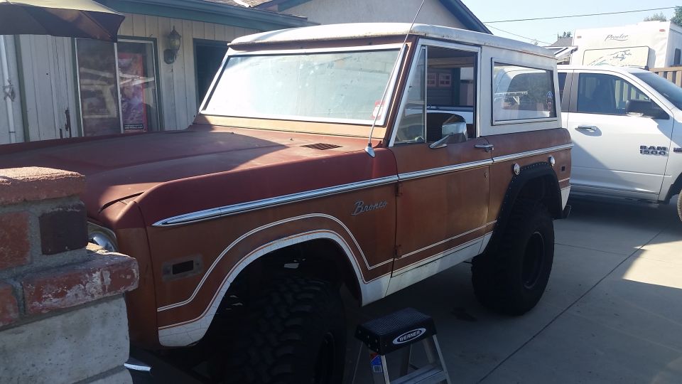 Brown and white early Ford Bronco SUV parked in driveway, 3/4 front view