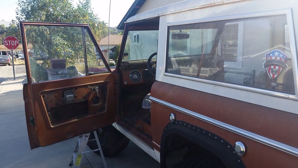 1973 Ford Bronco with driver's door open, showing interior and exterior.