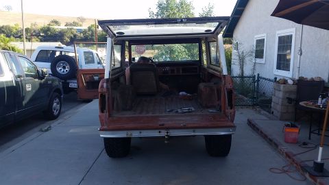 1973 Ford Bronco - The rear view of a vintage Ford Bronco with its tailgate and hardtop open. The vehicle is orange and appears to be undergoing restoration,…