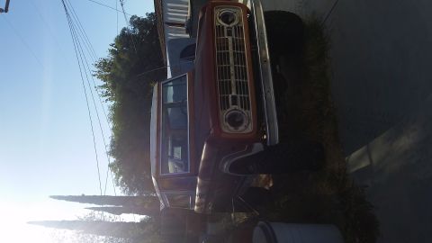 1973 Ford Bronco - Rotated photo of a red and white vintage truck with round dual headlights and chrome grille parked along a road.