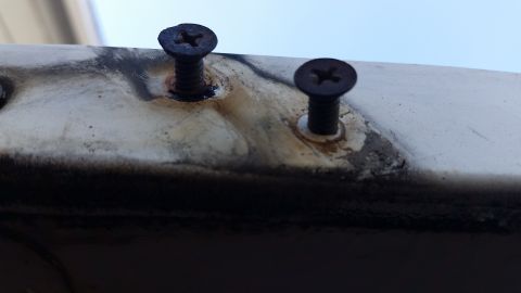 1973 Ford Bronco - Two rusty Phillips head screws are visible on a weathered, off-white surface, possibly a vehicle panel. The screws are dark brown and show…
