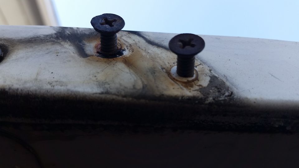 Two rusty screws on a weathered off-white surface.
