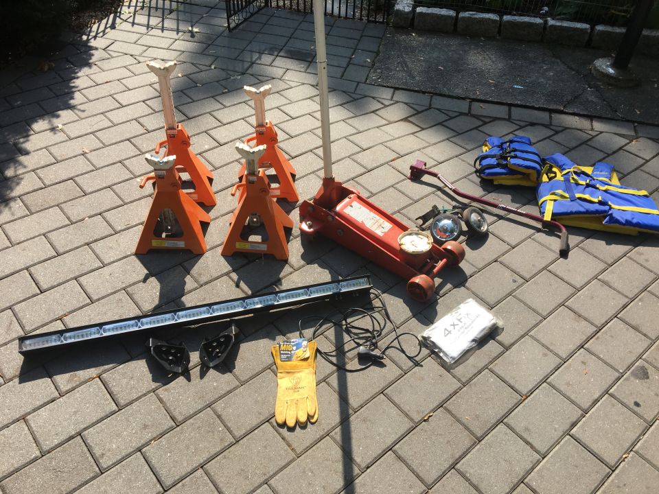 Car jack, jack stands, work gloves, LED light bar, and life vests laid out on a paved surface