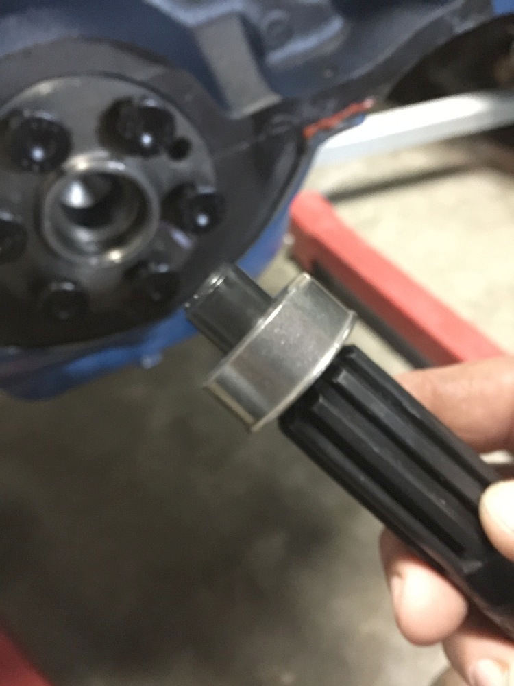 Hand holding a splined shaft with a metal ring against a dark, out-of-focus background with a blue component and red support