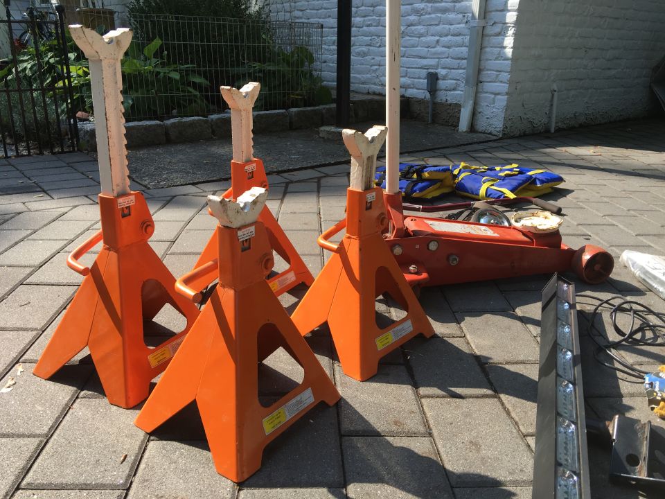 Four orange jack stands and a red floor jack on a paved surface