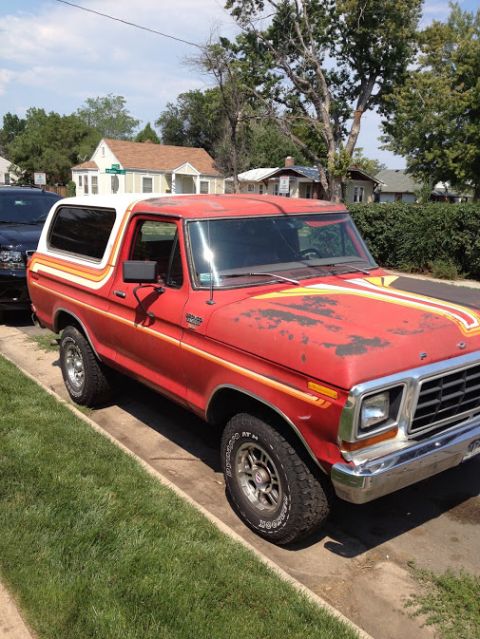 1978 Ford Bronco - This red 1978 Ford Bronco is parked on a residential street, showing its distinctive racing stripes and white camper shell.