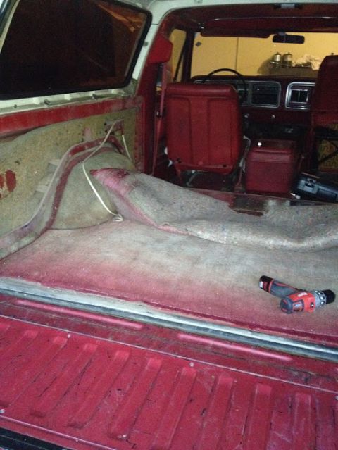 1978 Ford Bronco - The interior of a red 1978 Ford Bronco shows a worn carpet and seats, with a visible dashboard and cargo area.