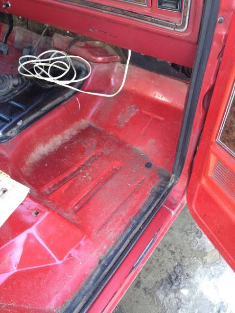 1978 Ford Bronco - Interior view of a red vehicle's floor, showing a coiled white wire and a black gear shifter.