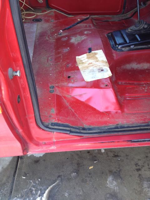 1978 Ford Bronco - The interior floor of a red vehicle shows a taped document and a gear shifter base.