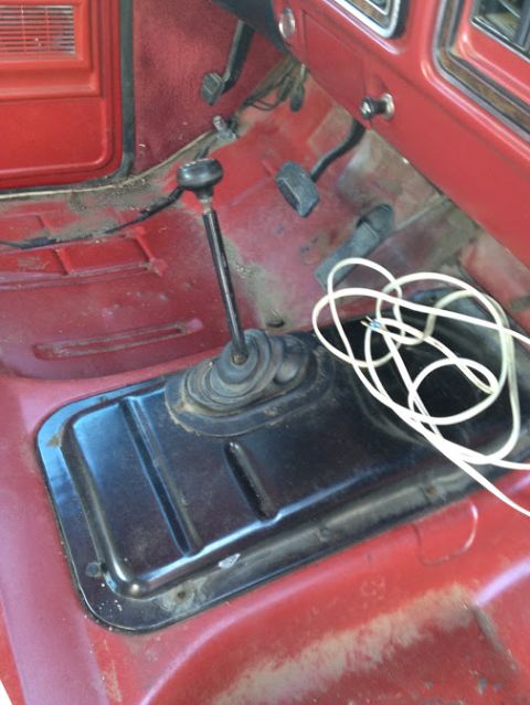 1978 Ford Bronco - The interior floor of a vehicle shows a manual transmission shifter and pedals, with a white cord resting on the transmission tunnel.
