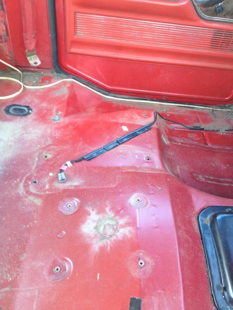 1978 Ford Bronco - Interior view of a vehicle's red floor and door panel, showing exposed wiring and mounting holes.