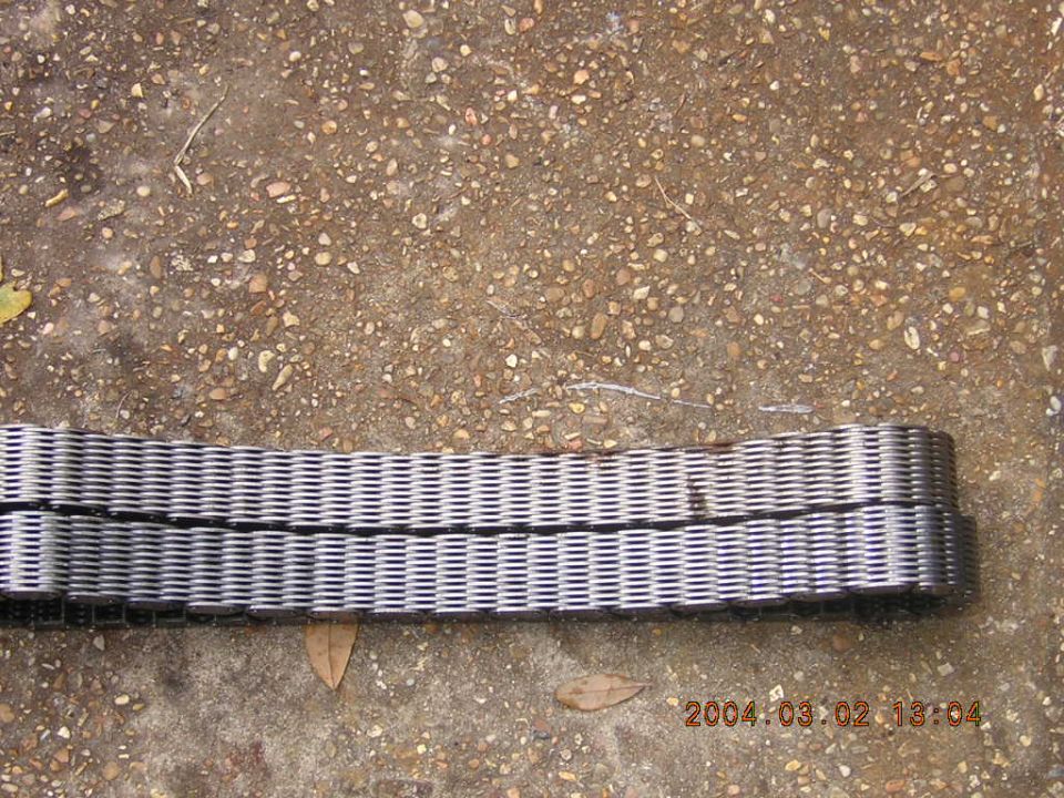 Double-row metal timing chain lying on gravel ground