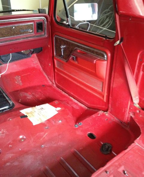 1978 Ford Bronco - The interior of a red truck is shown, with the door panel and dashboard visible. The floor is bare and red.