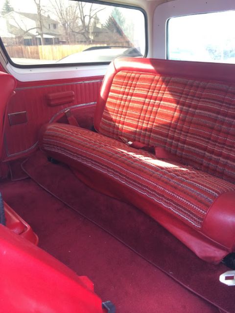 1978 Ford Bronco - The interior of a vehicle features red carpeting and plaid seat covers, with a view of a residential area through the window.
