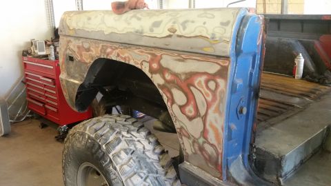 1979 Ford Bronco - The body of a Ford Bronco is undergoing repairs, showing primer, body filler, and a large off-road tire.