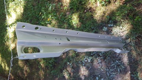 1994 Ford Bronco - A single metal car part is shown resting on a grassy area, likely a component from a vehicle's chassis.