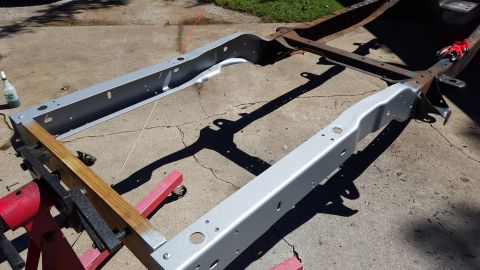 1994 Ford Bronco - A vehicle frame is shown on jack stands, with parts of it freshly painted silver, indicating restoration work.