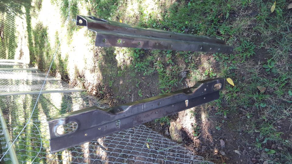 Two dark metal car frame sections on grass, one with a circular cutout