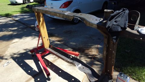 1994 Ford Bronco - Vehicle frame undergoing restoration, supported by an engine stand, with two modern cars visible in the background.