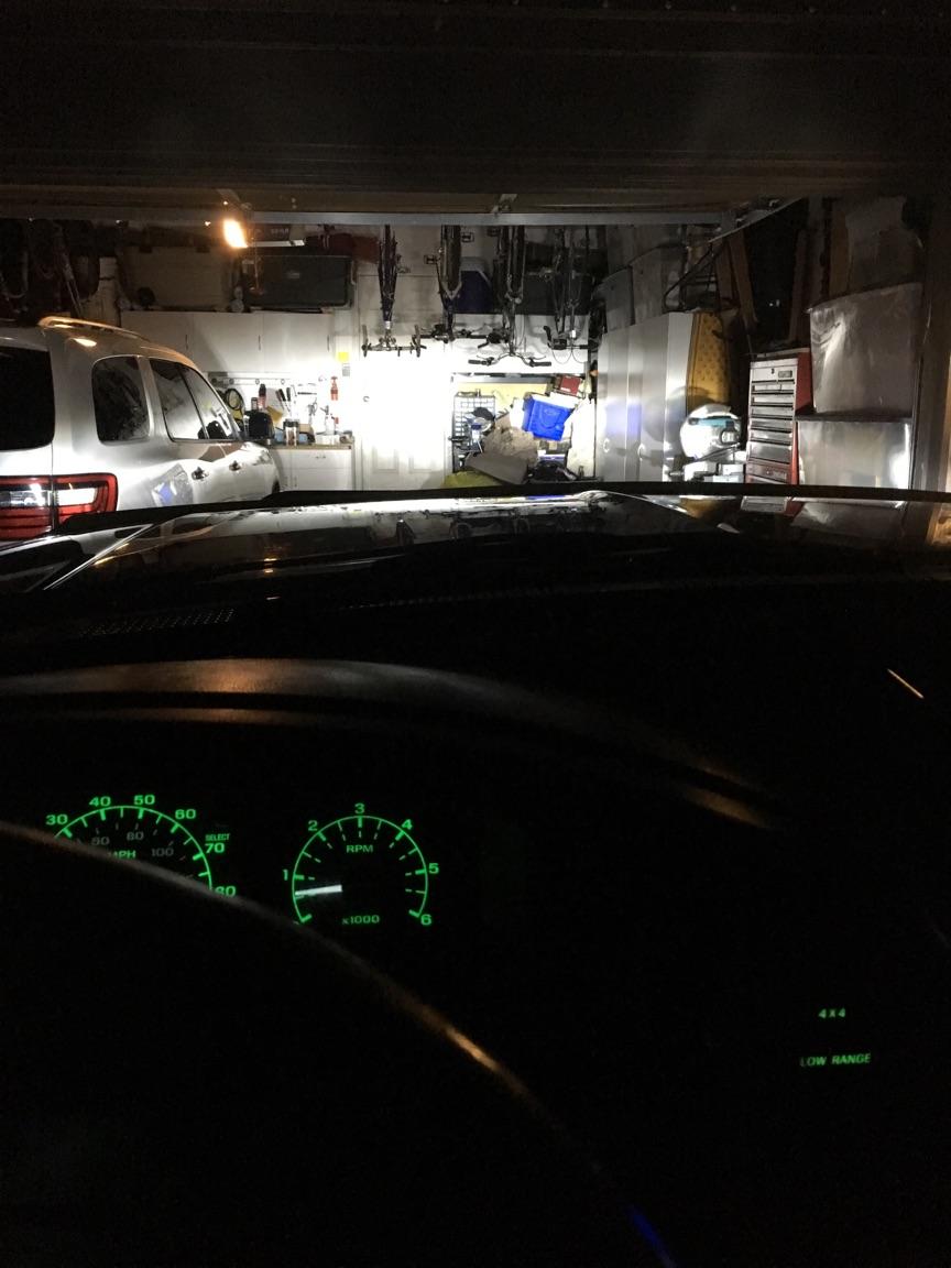 View from inside a vehicle looking out at a white SUV in a garage. Dashboard gauges are lit up green