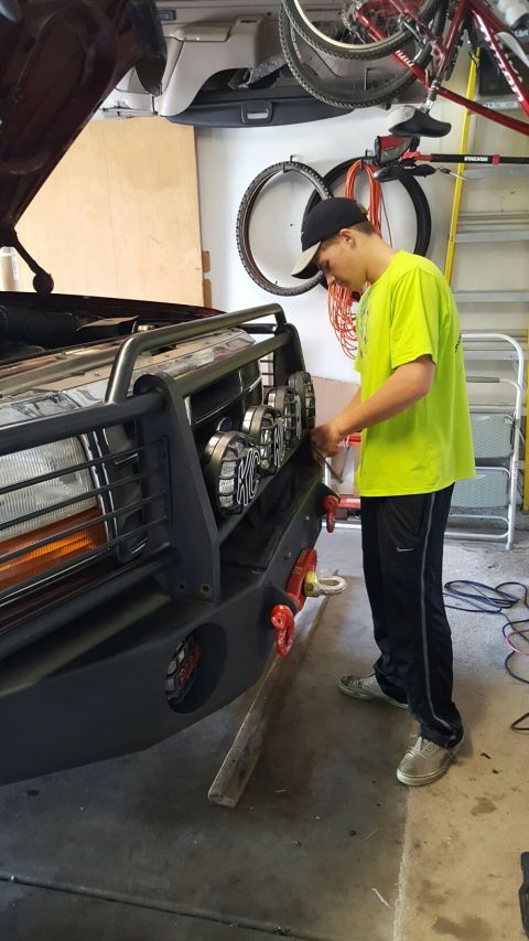 1996 Ford Bronco - Person works on a custom front bumper with KC lights and red tow hooks.