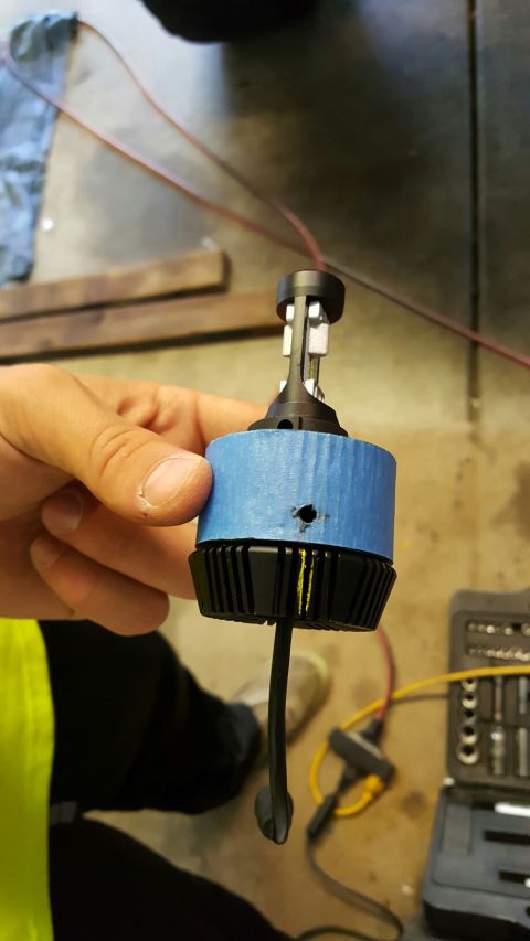 1996 Ford Bronco - A person is holding an LED headlight bulb, which is partially wrapped in blue tape.