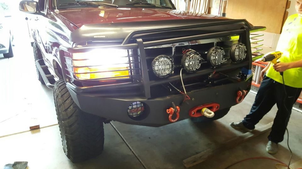 1996 Ford Bronco front end with custom bumper, KC lights, and tow hooks. A person is visible on the right holding a heat gun