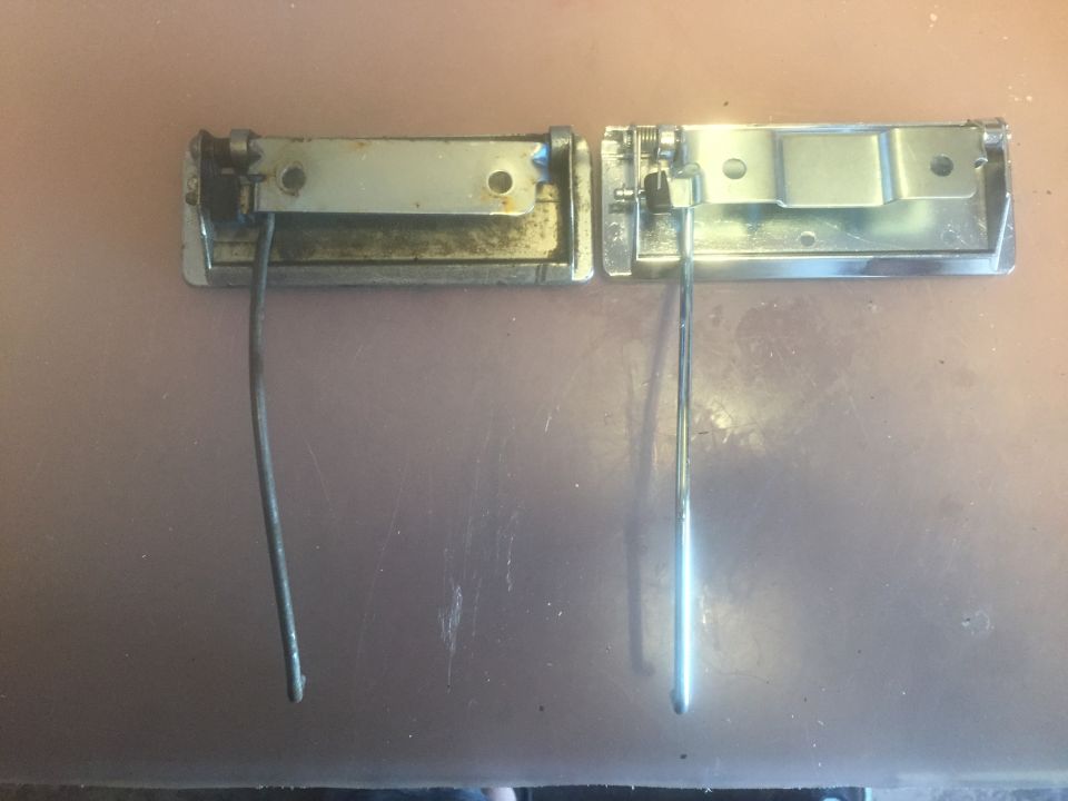 Two chrome door handles with linkage rods against a brown surface