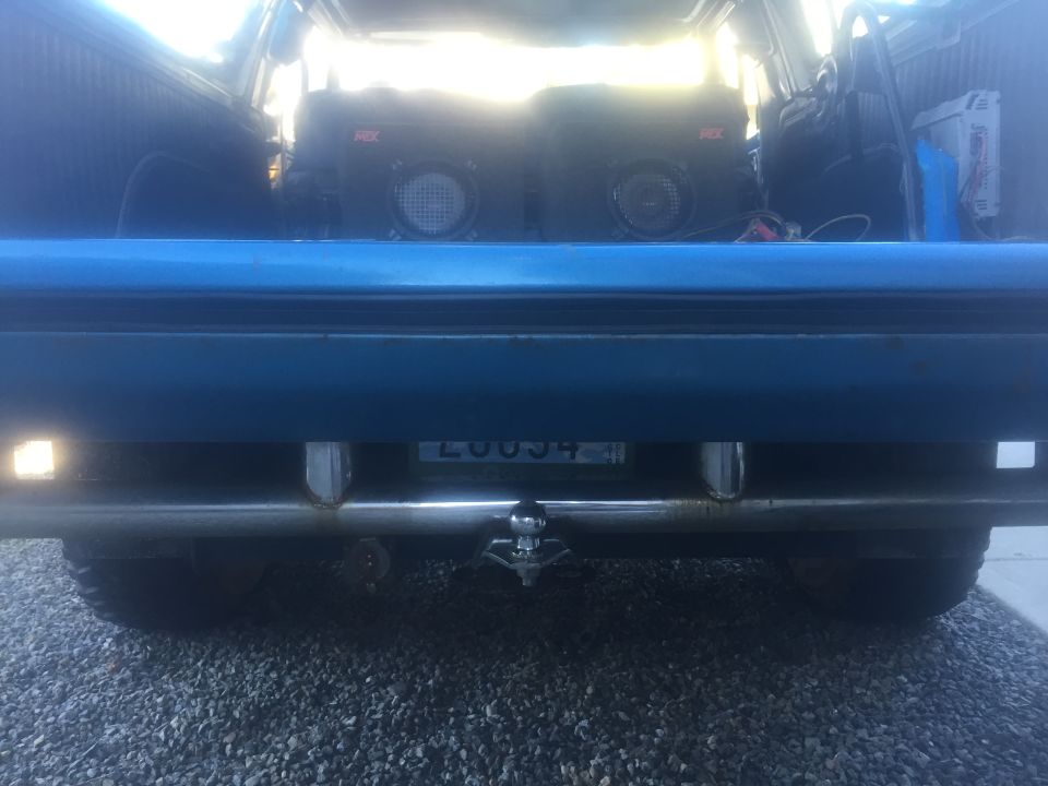 Rear view of a blue SUV showing a trailer hitch and two aftermarket speakers inside the cargo area. License plate reads LUU034