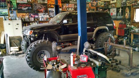 1985 Jeep CJ7 - A heavily modified black Toyota 4Runner is elevated on a lift in a cluttered garage.