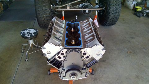 1985 Jeep CJ7 - A V8 engine is displayed on a stand, with a portion of a Jeep's chassis and tire visible in the background.
