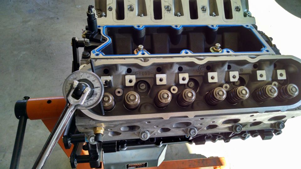 Engine cylinder head on an orange stand with a torque wrench measuring valve spring pressure