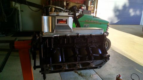 1985 Jeep CJ7 - An engine block sits on a stand, with a lawnmower visible behind it in a garage.