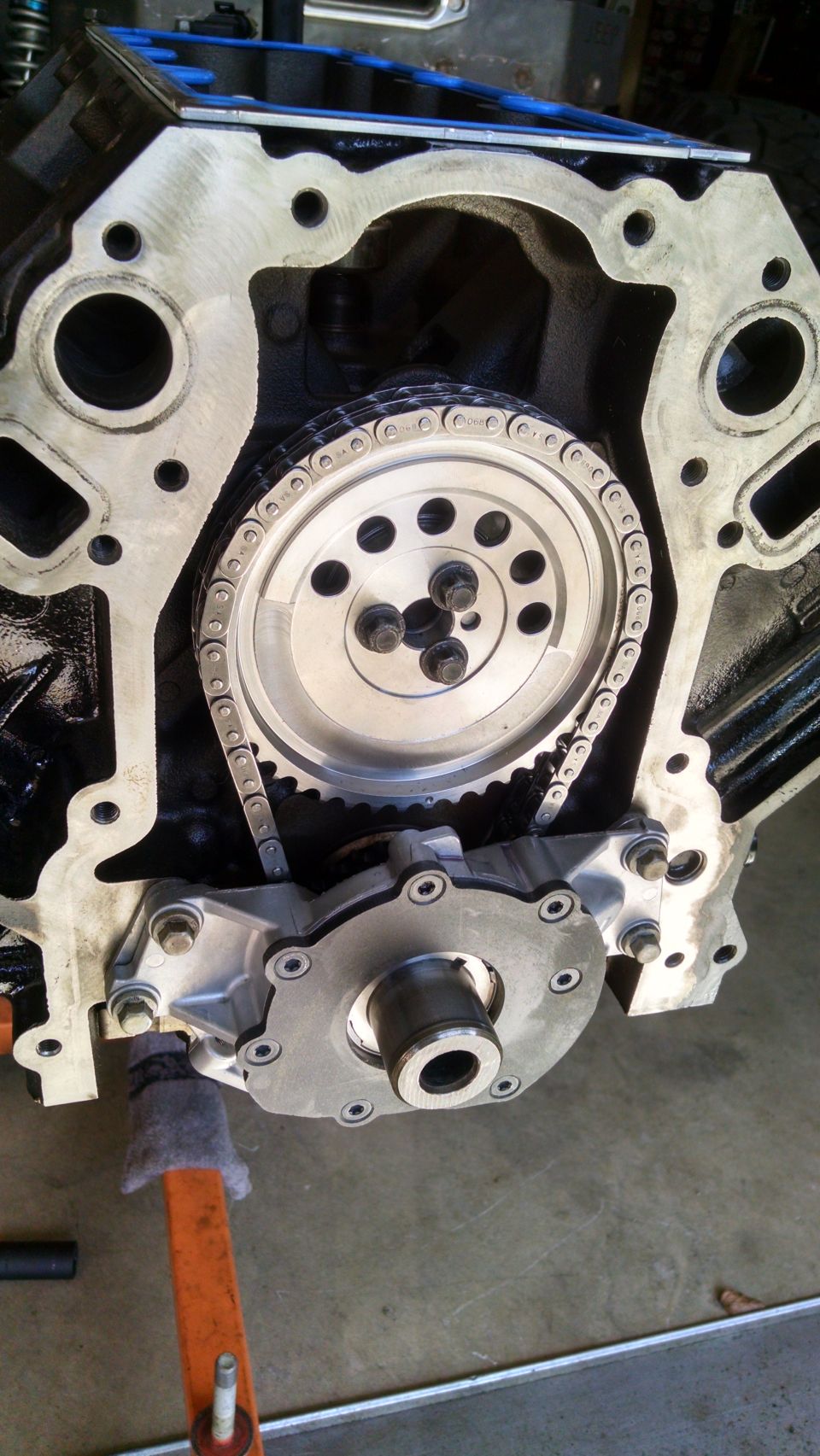 Engine block with timing chain, gears, and oil pump assembly mounted. Gray metal components against black engine block