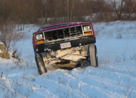 1981 Ford Bronco - A red Jeep Cherokee XJ is driving through deep snow, with one wheel significantly higher than the others.