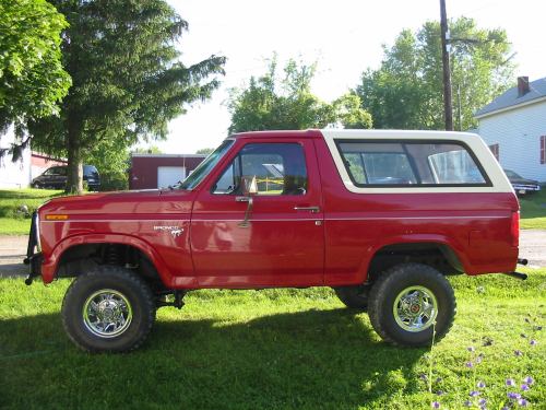 Red Ford Bronco with white top, lifted with chrome wheels, side view parked on grass