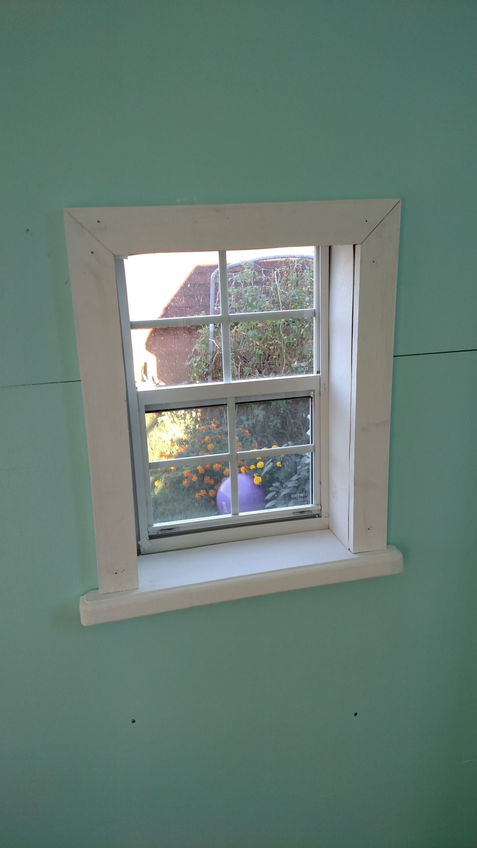Playhouse window looking out onto a garden with orange flowers and a purple ball