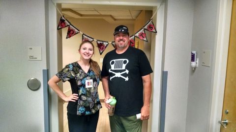 1985 Jeep CJ7 - A woman in scrubs and a man wearing a black t-shirt with a Jeep skull graphic stand in a hallway decorated with a banner.