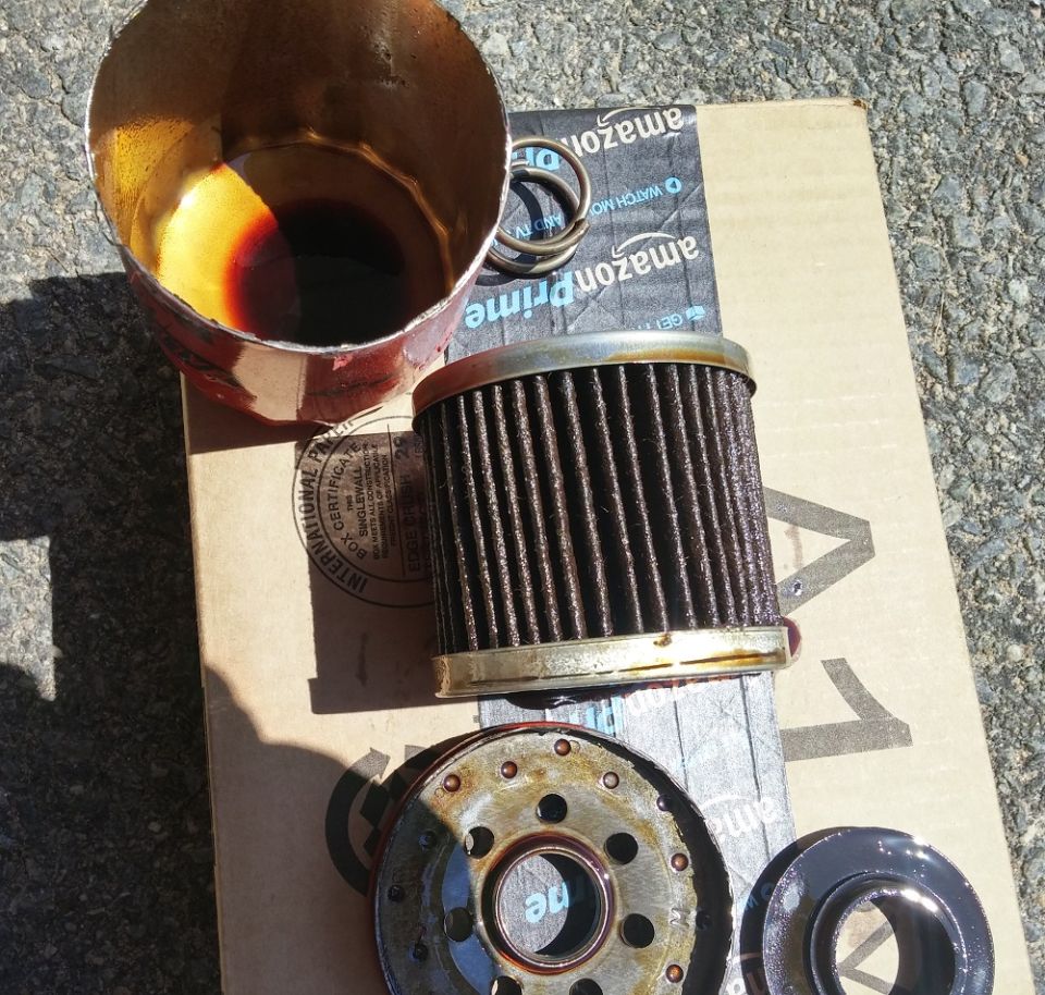 Used oil filter and cup with oil on a cardboard box.