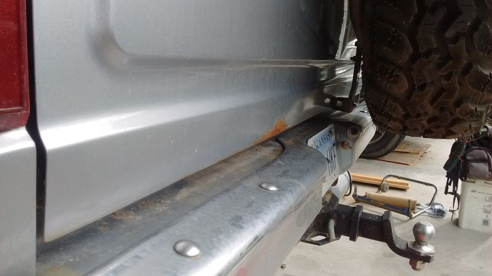 Rear bumper and quarter panel of a silver SUV with a spare tire and trailer hitch.