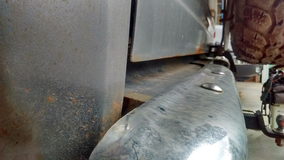 Close-up of rusted rear bumper and lower body panel of a vehicle with a spare tire above.