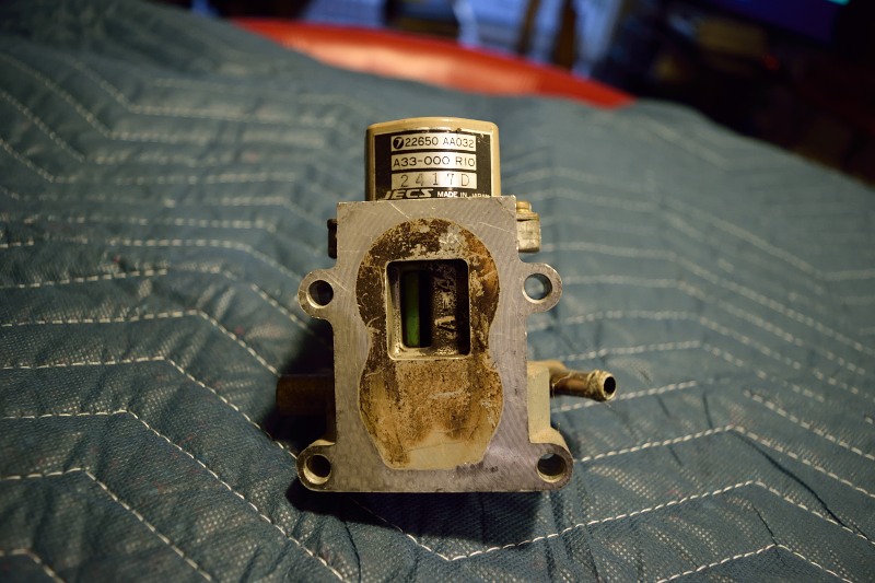 Automotive emissions control valve with label, resting on blue quilted surface.