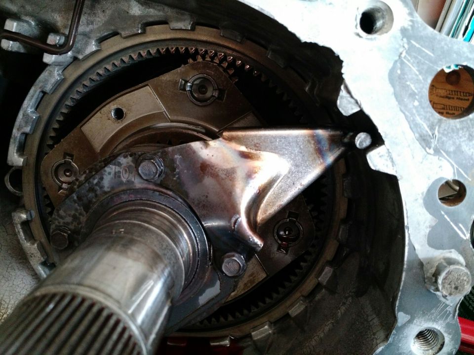 Internal view of a transmission showing gears, shaft, and damaged metal plate.