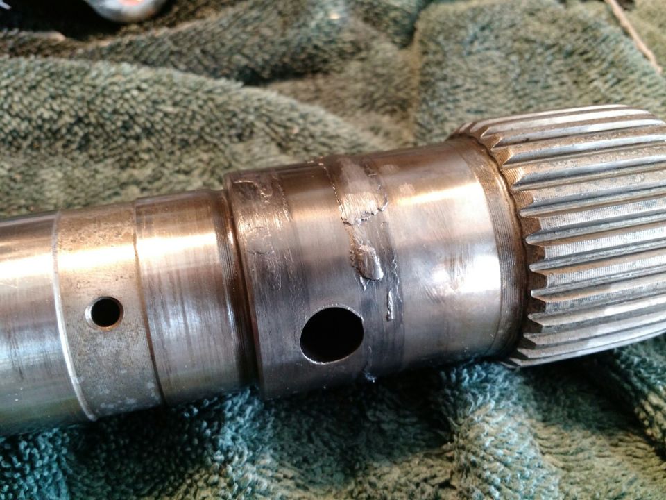Close-up of a metal splined shaft with two drilled holes, resting on a green textured cloth.