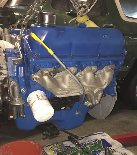 1978 Ford Bronco - A blue Ford V8 engine is shown, suspended by chains, with a silver exhaust manifold and a white oil filter attached. The engine appears to…
